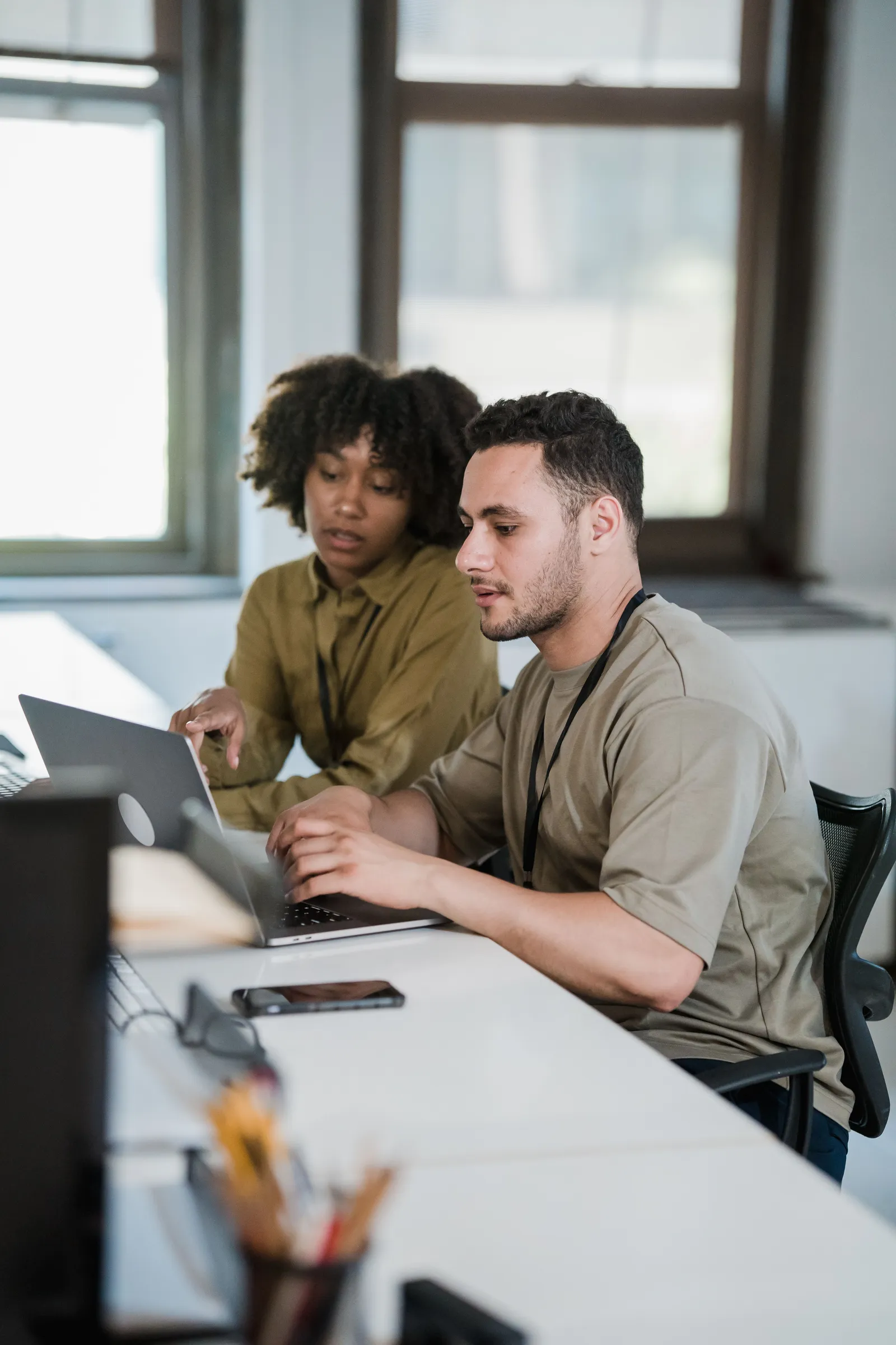 Two colleagues working through something on a laptop at a bright desk