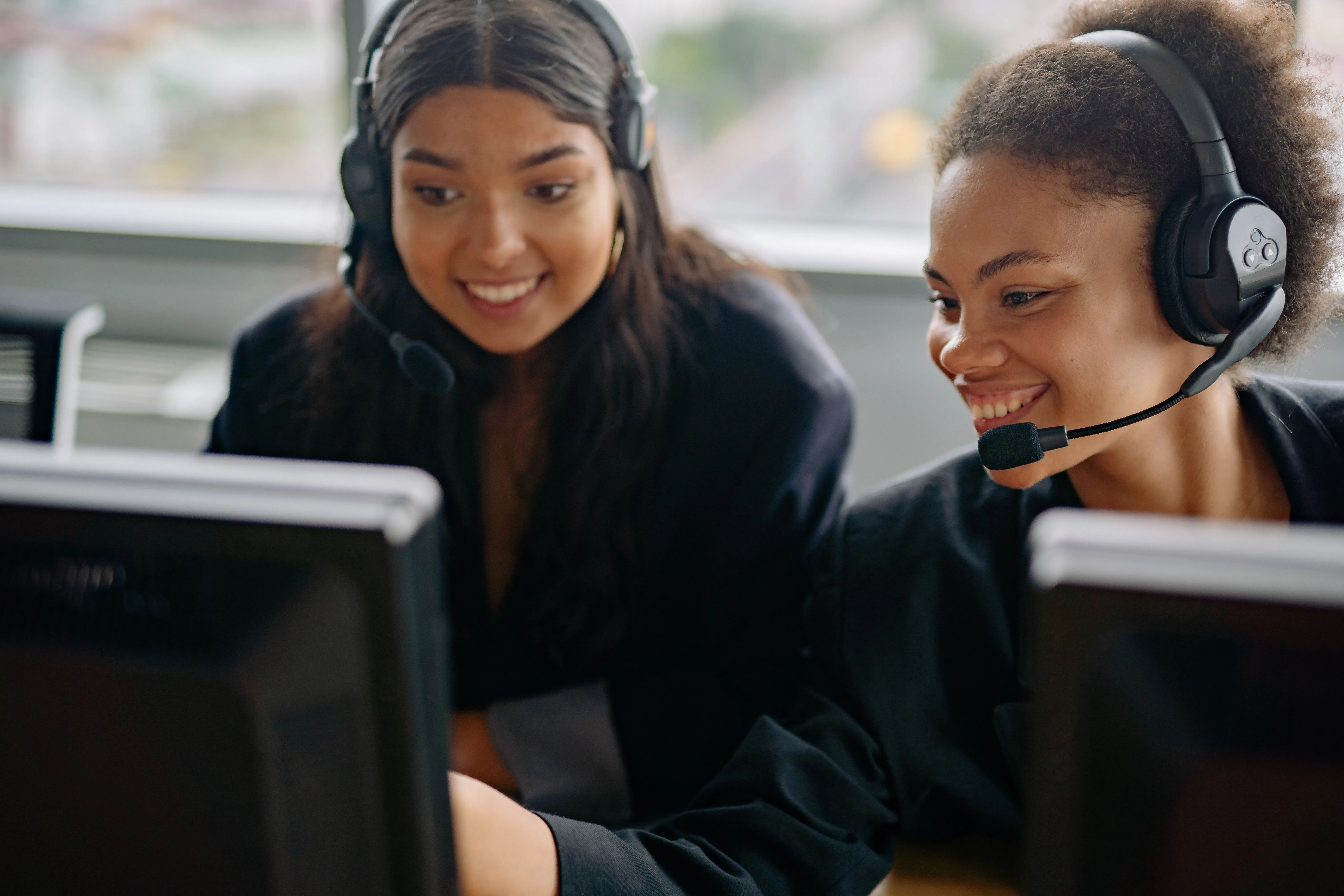 Two women wearing headsets learning together at computers