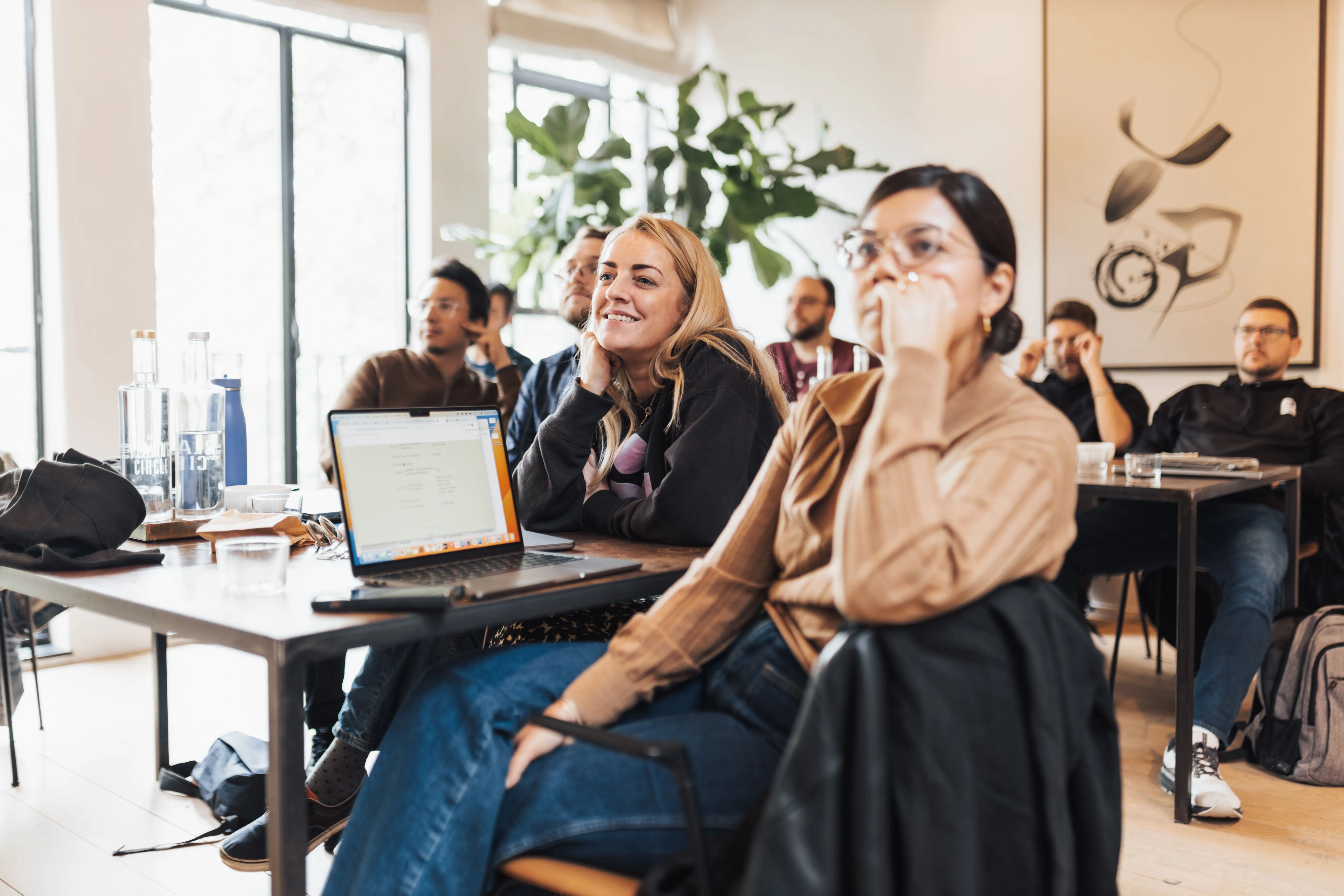 Workshop participants smiling and following along on laptops in a bright community space